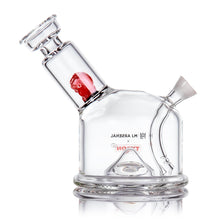 A clear borosilicate glass MJ Arsenal x Tyson 2.0 Punch-Out bubbler featuring a tilted cylindrical neck, red glass accent inside, and the LM ARSENAL x TROJAN logo printed in reverse on the body.