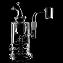 The MJ Arsenal Ursa Mini Dab Rig, made from clear borosilicate glass with a cylindrical base, bent neck, and attached quartz banger, is displayed against a black background.