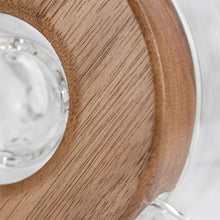 Close-up of a circular wooden handle attached to clear glass, highlighting the wood grain and part of the MJ Arsenal Alpine Series - Apex Mini Rig against a light background.