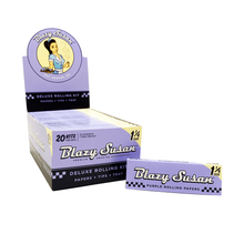 A box display of Blazy Susan Purple Rolling Papers 1 1/4 size, featuring vibrant purple papers, tips, and a tray. One individual deluxe rolling kit is shown in front of the packaging.