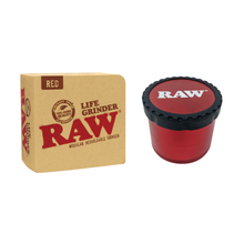 A red RAW Life Grinder, crafted from aircraft-grade aluminum with a black lid labeled RAW, is displayed next to its brown packaging marked RAW Life Grinder and Red.
