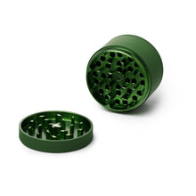 The Human Grade Grinder 4R (2.5") is a green, 4-piece grinder with sharp teeth in both the lid and base and features a pollen catcher for fine herbs. Shown with the lid off on a white surface.