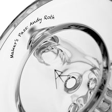 A close-up of the MJ Arsenal Bloopcycler Dab Rig, a clear glass piece with smooth curves and reflections. "Maker’s Pass: Andy Roth" is printed on the rim, with an arrow symbol by a small hole to enhance your dabbing experience.