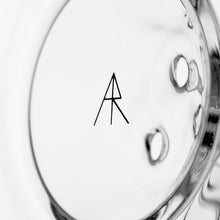 A black geometric “A” and “R” logo intertwines at the center of a glossy, abstract, transparent surface with curved shapes and light reflections, echoing MJ Arsenal Bloopcycler Dab Rig’s refined style against a mostly white and silver backdrop.