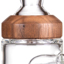 A close-up of the MJ Arsenal Alpine Series - Halo Peak Top shows its clear borosilicate glass body with an upgraded transparent finish, accented by a natural wood collar featuring smooth grain that contrasts elegantly with the glass.