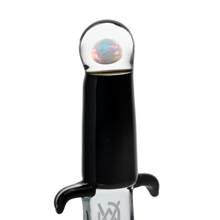 A close-up of the MJ Arsenal Excalibur Dab Tool, made from borosilicate glass, featuring a black grip, two short crossguards, and a clear orb at the top with an iridescent sphere inside from the Dragon Series.