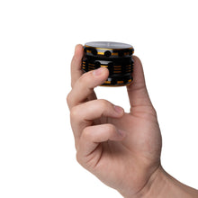 A hand holds the Human Grade Grinder 5T (2.5"), a compact aluminum grinder featuring a round black and yellow design with circular grooves, isolated on a white background.